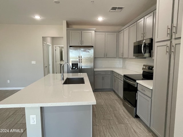 kitchen featuring gray cabinets, sink, a kitchen island with sink, and stainless steel appliances