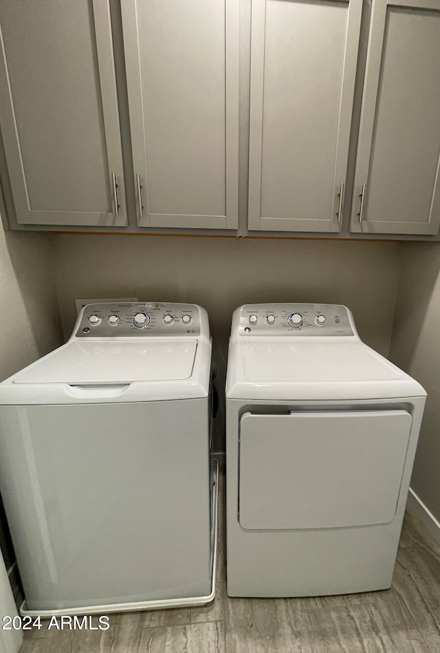 clothes washing area with light hardwood / wood-style floors, washing machine and dryer, and cabinets