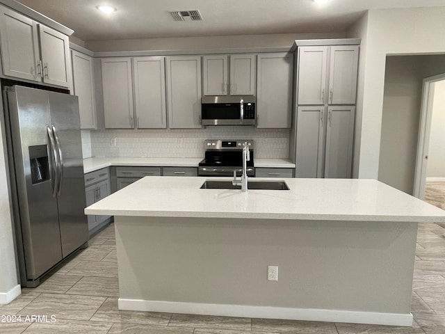 kitchen featuring tasteful backsplash, a center island with sink, appliances with stainless steel finishes, gray cabinets, and sink