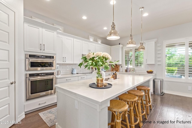 kitchen with a kitchen island, backsplash, white cabinets, and pendant lighting