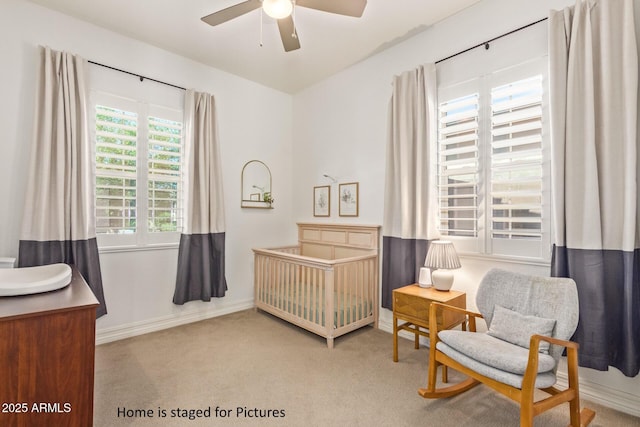 bedroom with ceiling fan, a nursery area, and light carpet