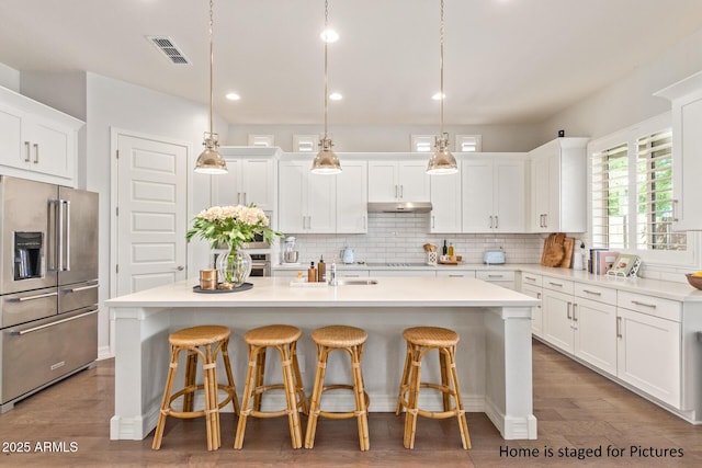 kitchen featuring decorative light fixtures, white cabinets, a kitchen island with sink, and high end fridge