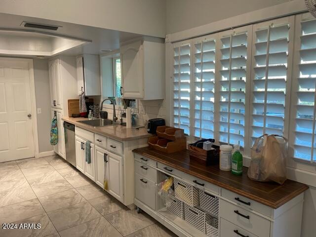 kitchen featuring sink, stainless steel dishwasher, wooden counters, backsplash, and white cabinets