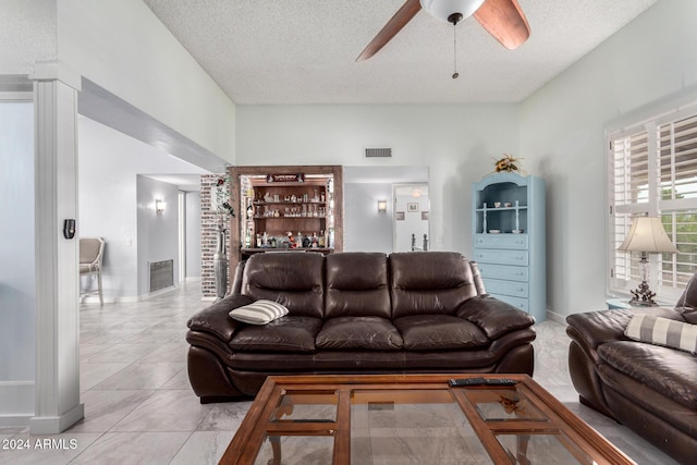 tiled living room with ceiling fan, indoor bar, and a textured ceiling