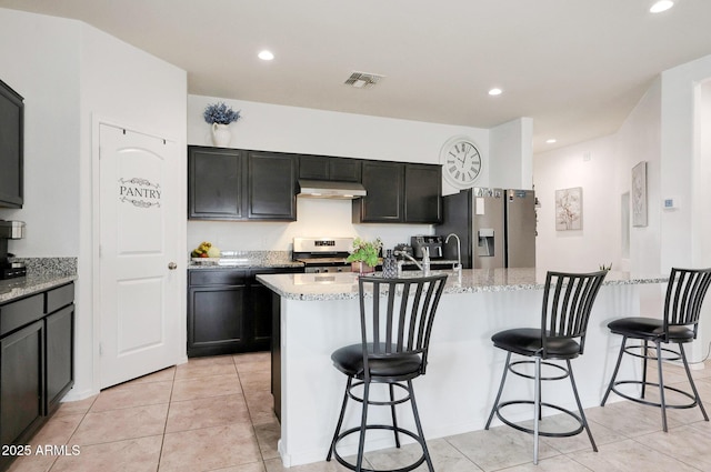 30777 W Whitton Ave, Buckeye, AZ 85396 - kitchen featuring appliances with stainless steel finishes, under cabinet range hood, an island with sink, light stone countertops, and light tile patterned flooring