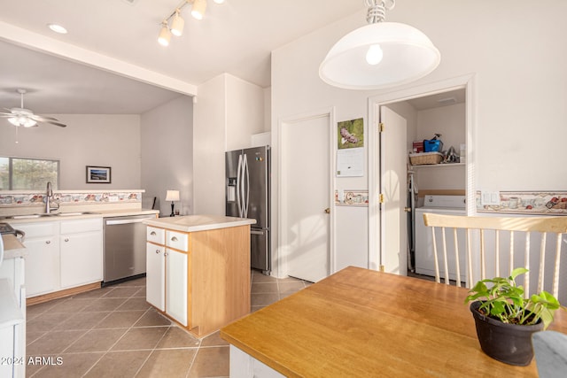 kitchen with appliances with stainless steel finishes, pendant lighting, white cabinets, washer / clothes dryer, and a kitchen island