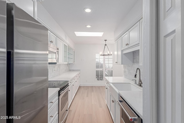 kitchen featuring a skylight, stainless steel appliances, light wood-type flooring, and light countertops