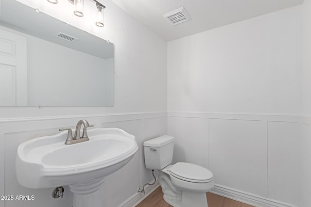 half bath featuring a wainscoted wall, toilet, and visible vents