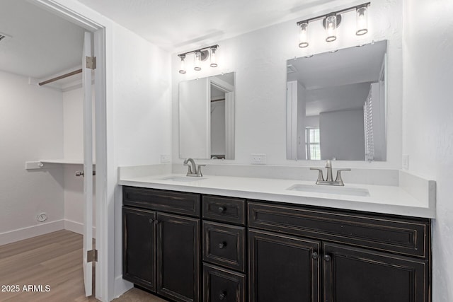 bathroom featuring double vanity, wood finished floors, baseboards, and a sink