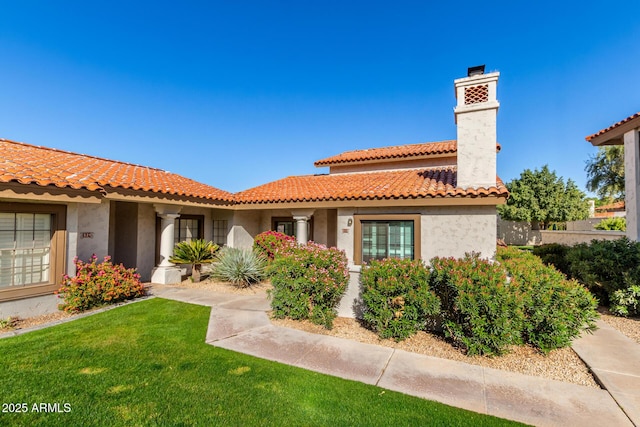 mediterranean / spanish home featuring stucco siding, a front lawn, a chimney, and a tiled roof