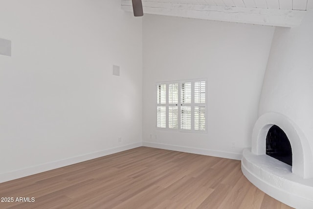 unfurnished living room featuring light wood finished floors, baseboards, beamed ceiling, wood ceiling, and a towering ceiling