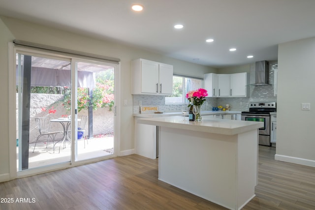 kitchen featuring hardwood / wood-style floors, white cabinetry, stainless steel range with electric cooktop, a center island, and wall chimney exhaust hood