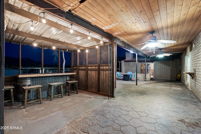 basement featuring ceiling fan, brick wall, and bar area