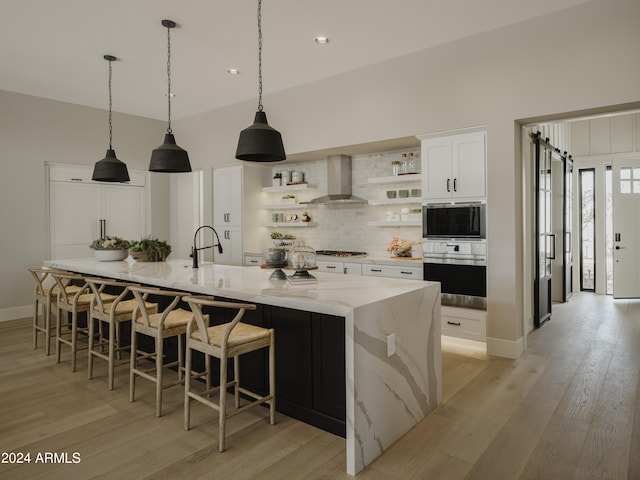 kitchen with wall chimney range hood, light hardwood / wood-style floors, white cabinetry, appliances with stainless steel finishes, and a large island