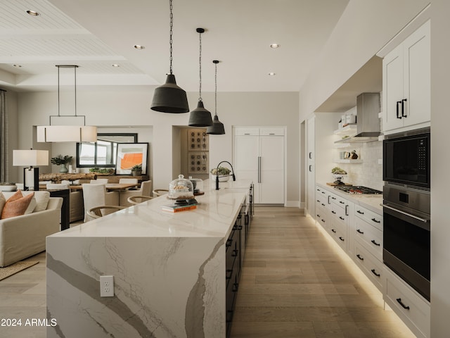 kitchen with light hardwood / wood-style floors, a large island with sink, light stone counters, hanging light fixtures, and appliances with stainless steel finishes