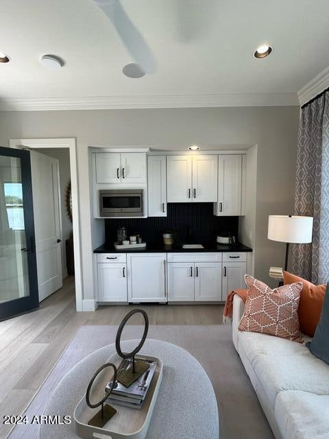 kitchen featuring crown molding, tasteful backsplash, light wood-type flooring, stainless steel microwave, and white cabinets