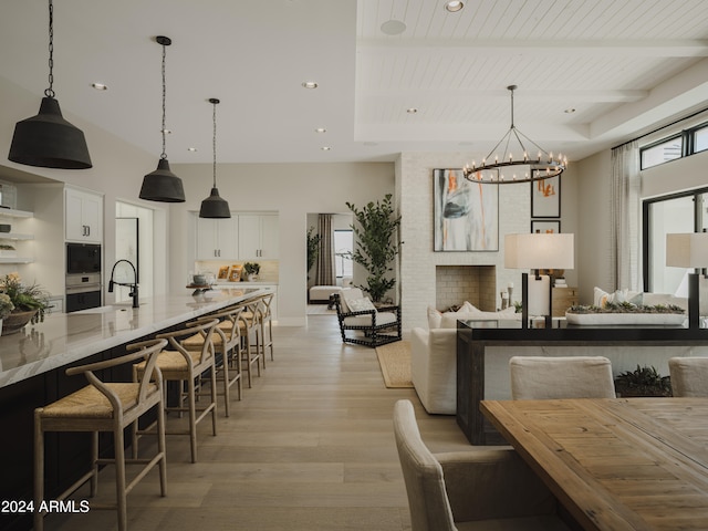 dining space featuring light hardwood / wood-style flooring, wooden ceiling, a chandelier, sink, and a raised ceiling