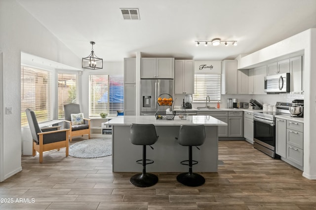 kitchen with appliances with stainless steel finishes, gray cabinetry, sink, pendant lighting, and a center island