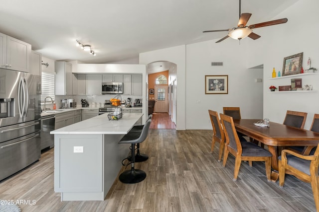 kitchen featuring sink, stainless steel appliances, gray cabinets, a kitchen island, and light wood-type flooring