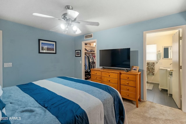 carpeted bedroom featuring a walk in closet, ensuite bath, a closet, and ceiling fan