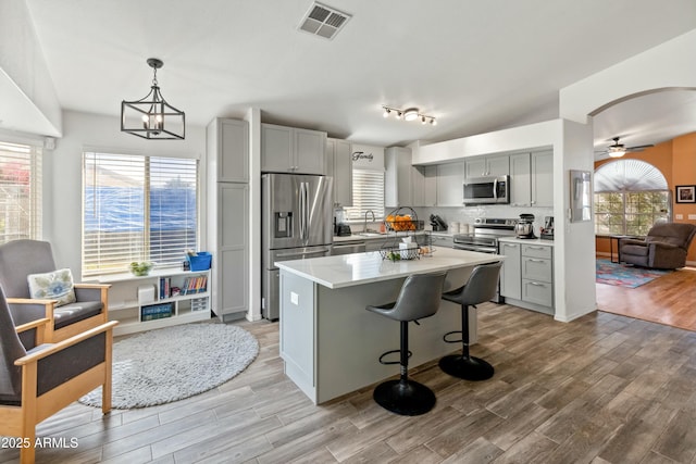 kitchen with gray cabinets, a center island, decorative light fixtures, and appliances with stainless steel finishes