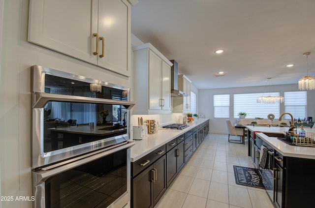 kitchen featuring wall chimney range hood, sink, white cabinetry, stainless steel appliances, and decorative light fixtures