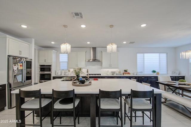 kitchen with stainless steel appliances, a spacious island, decorative light fixtures, and wall chimney exhaust hood