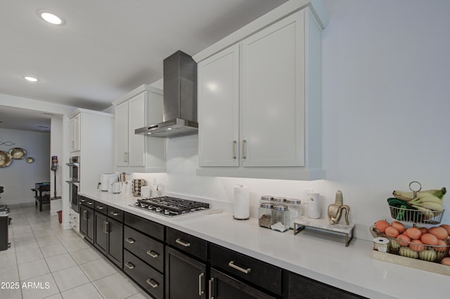 kitchen featuring white cabinetry, stainless steel appliances, light tile patterned floors, and wall chimney range hood