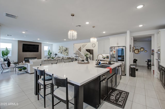 kitchen with light tile patterned floors, white cabinetry, hanging light fixtures, a kitchen island with sink, and stainless steel appliances