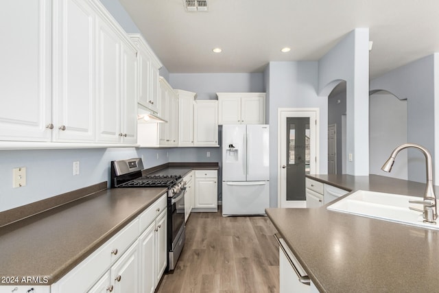 kitchen featuring white fridge with ice dispenser, stainless steel range with gas stovetop, white cabinets, and light wood-type flooring