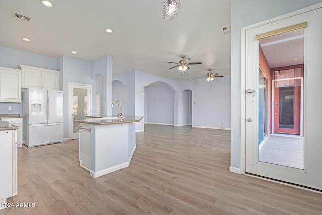 kitchen with light hardwood / wood-style floors, a center island with sink, white fridge with ice dispenser, white cabinets, and ceiling fan