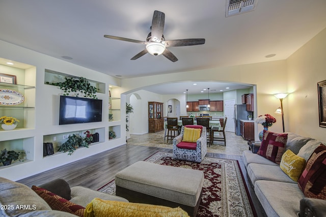 6554 W Rushmore Way, Florence, AZ 85132 - living room featuring arched walkways, built in shelves, ceiling fan, and light wood-style floors
