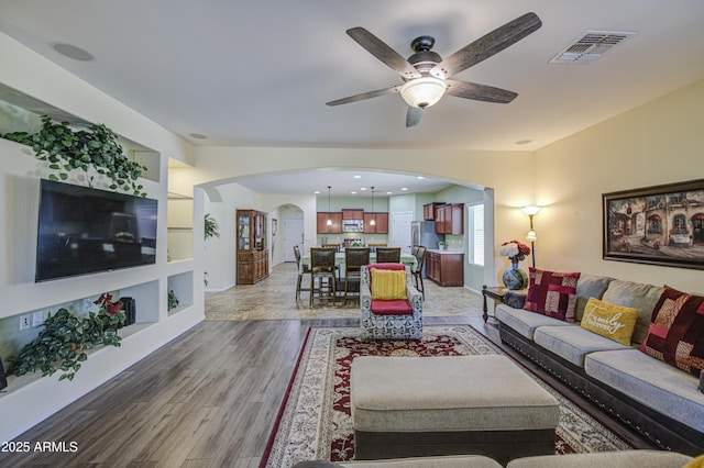 6554 W Rushmore Way, Florence, AZ 85132 - living room with arched walkways, light wood-style flooring, a ceiling fan, and built in shelves