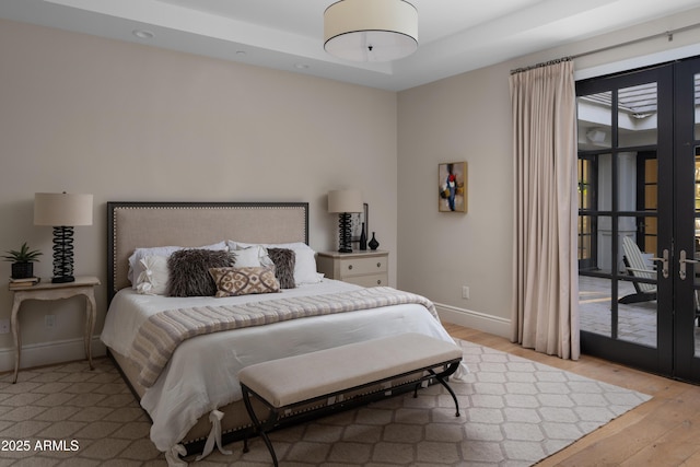 bedroom featuring french doors, a tray ceiling, and light hardwood / wood-style floors