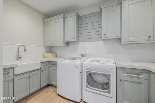 clothes washing area featuring sink, light hardwood / wood-style flooring, cabinets, and washer and dryer