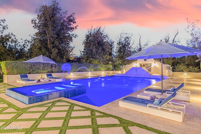 pool at dusk featuring a patio area and an in ground hot tub