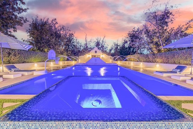 pool at dusk featuring pool water feature and a hot tub