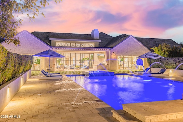 pool at dusk featuring pool water feature and a patio area