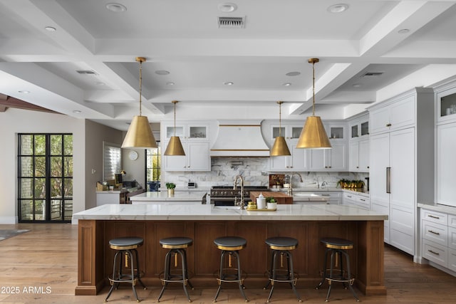 kitchen with a breakfast bar area, hanging light fixtures, a large island, light stone countertops, and custom range hood