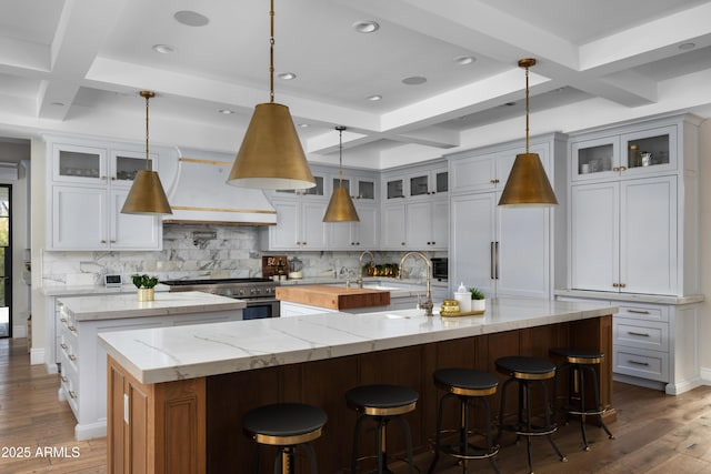 kitchen with a spacious island, premium range hood, white cabinetry, light stone counters, and hanging light fixtures