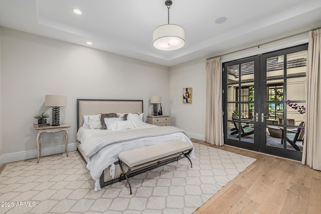 bedroom with french doors, a tray ceiling, light hardwood / wood-style floors, and access to exterior