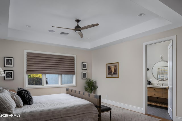 bedroom with a raised ceiling, ceiling fan, sink, and ensuite bath