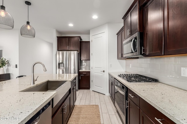 kitchen with sink, light stone countertops, appliances with stainless steel finishes, tasteful backsplash, and decorative light fixtures