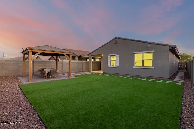 back house at dusk with a gazebo, a patio, and a lawn