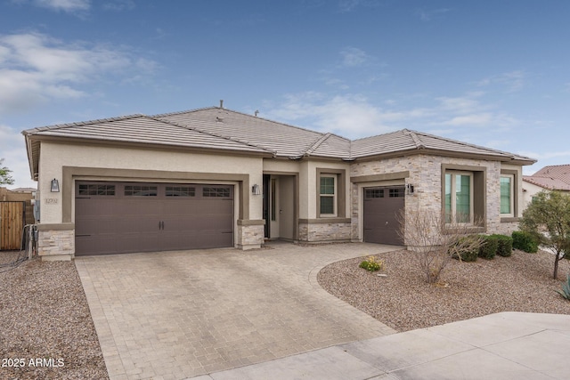 prairie-style house with an attached garage, stone siding, a tile roof, and decorative driveway