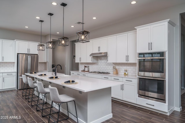 kitchen with visible vents, appliances with stainless steel finishes, wood tiled floor, a sink, and under cabinet range hood