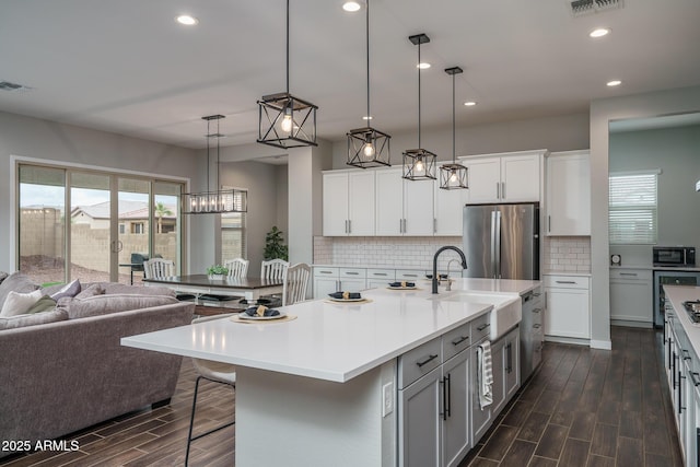 kitchen with open floor plan, freestanding refrigerator, wood tiled floor, black microwave, and a sink