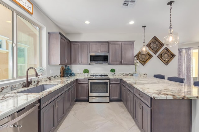 kitchen featuring appliances with stainless steel finishes, light stone counters, dark brown cabinets, sink, and pendant lighting