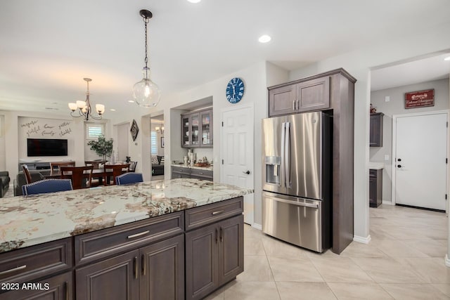 kitchen with dark brown cabinetry, light stone countertops, hanging light fixtures, stainless steel fridge with ice dispenser, and a chandelier