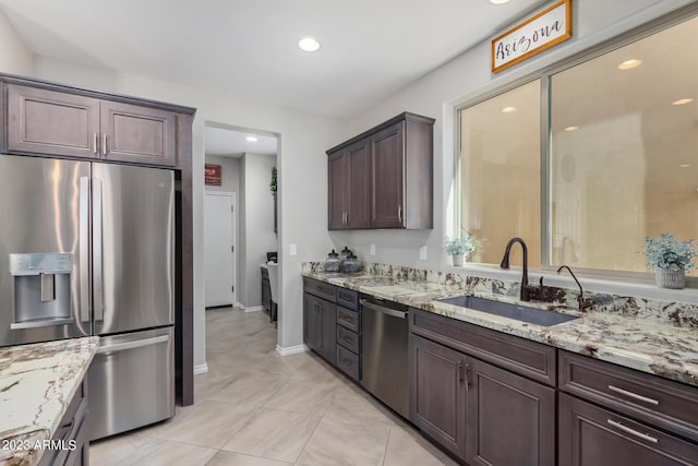 kitchen featuring dark brown cabinetry, stainless steel appliances, light stone counters, and sink